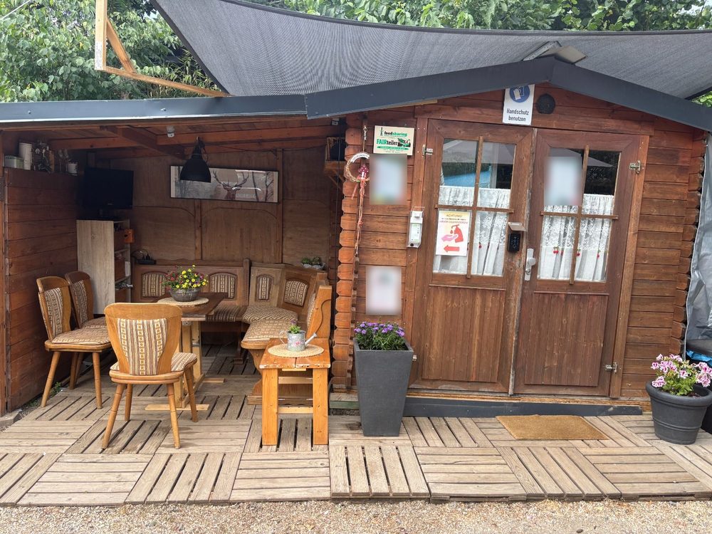 Teilerhütte mit überdachter Sitzecke und dem foodsharing-Fairteiler-Schild an der Tür